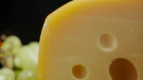 close up part of medium hard cheese head edam gouda parmesan on wooden board, with nuts and grapes rotaiting on the plate