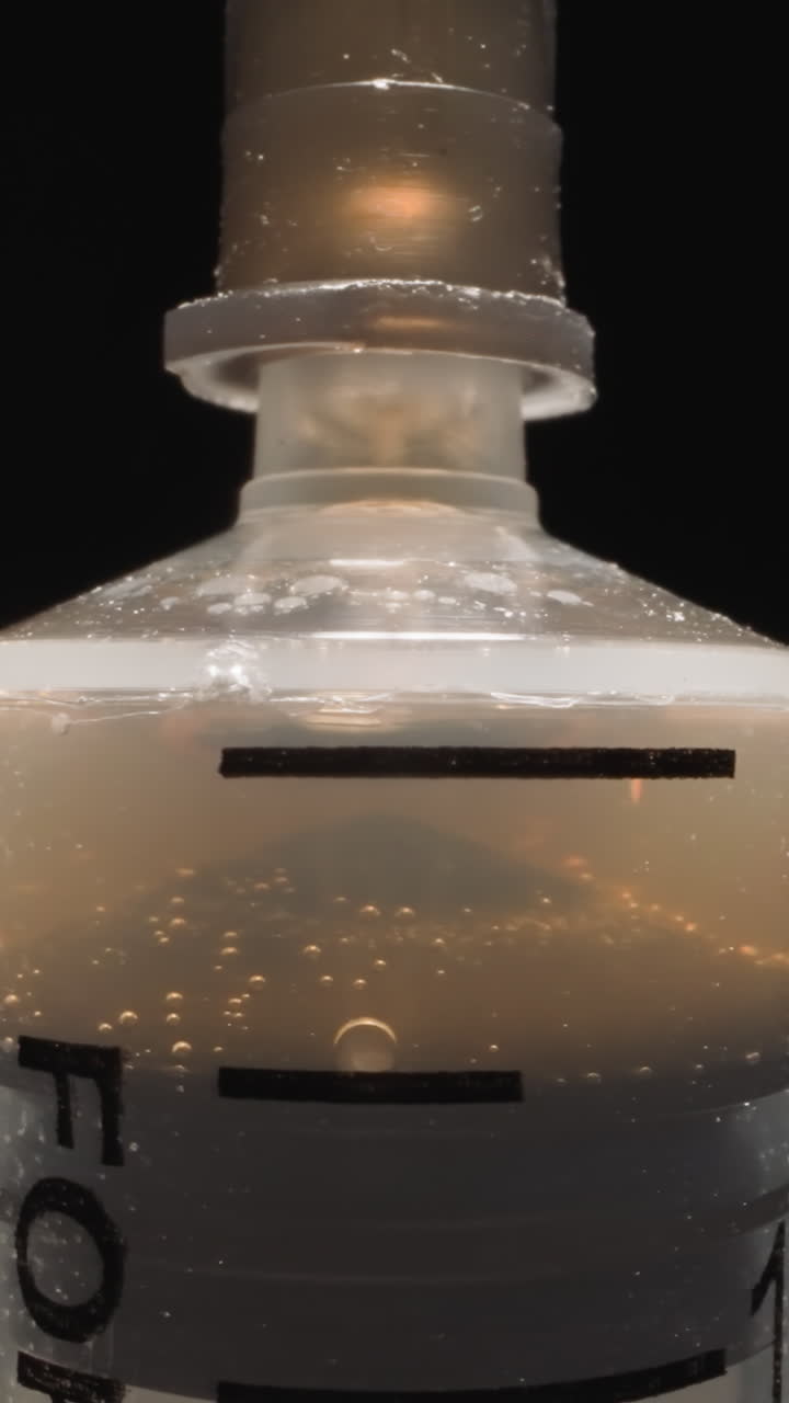 Plastic syringe with old liquid turning on black background. Tube with nozzle and piston for sucking in and ejecting liquid in thin stream macro