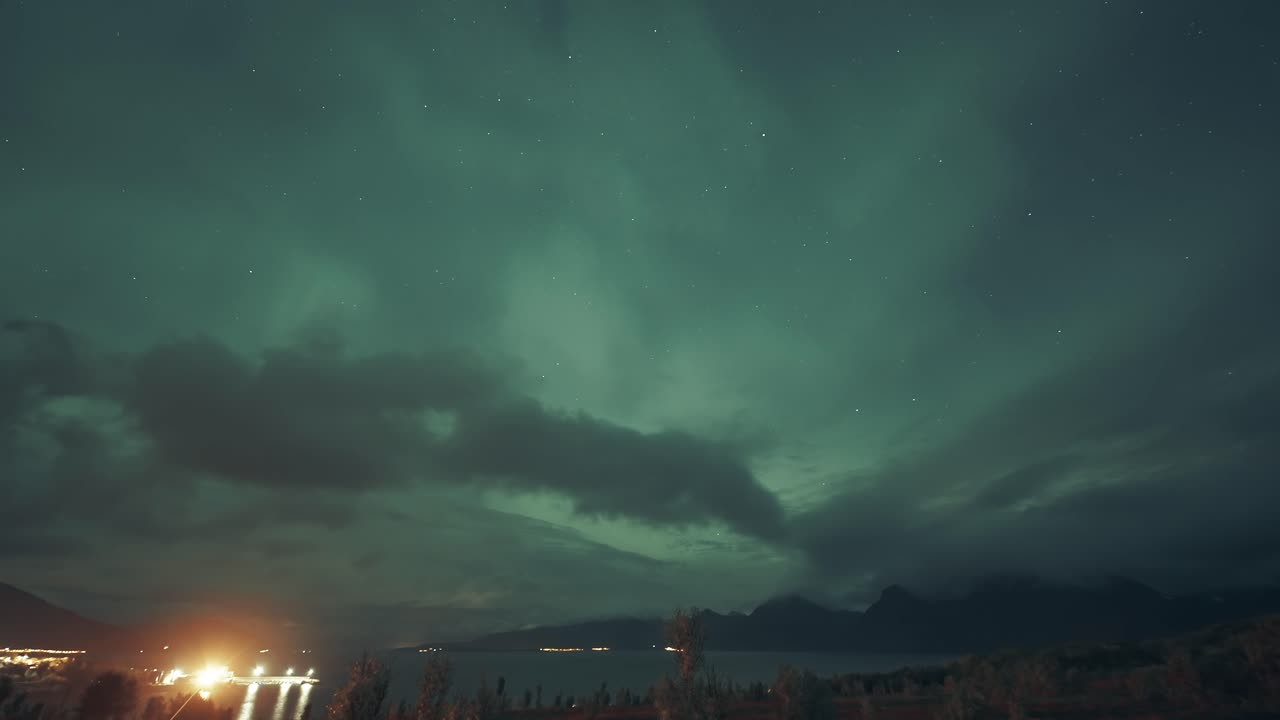 hipnotizante exhibición si las luces del norte en el cielo nocturno por encima de las aguas oscuras del fiordo y el puerto brillantemente iluminado