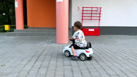 lovely smiling kid riding on his toy car. happy kid moves quickly by the paved road.