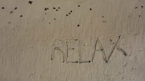 Aerial-camera-descending-onto-RELAX-inscribed-into-the-sand-on-a-beach