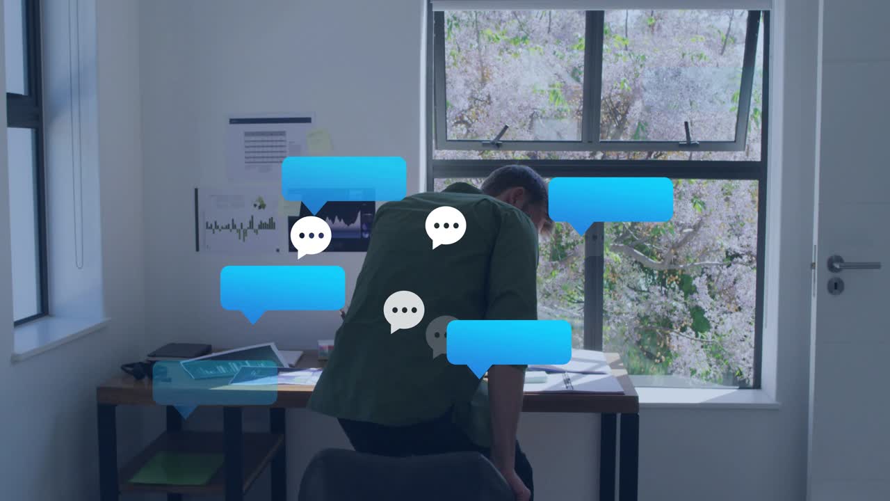 Man at desk sitting after blue chat bubble popping, answering phone and working laptop for business