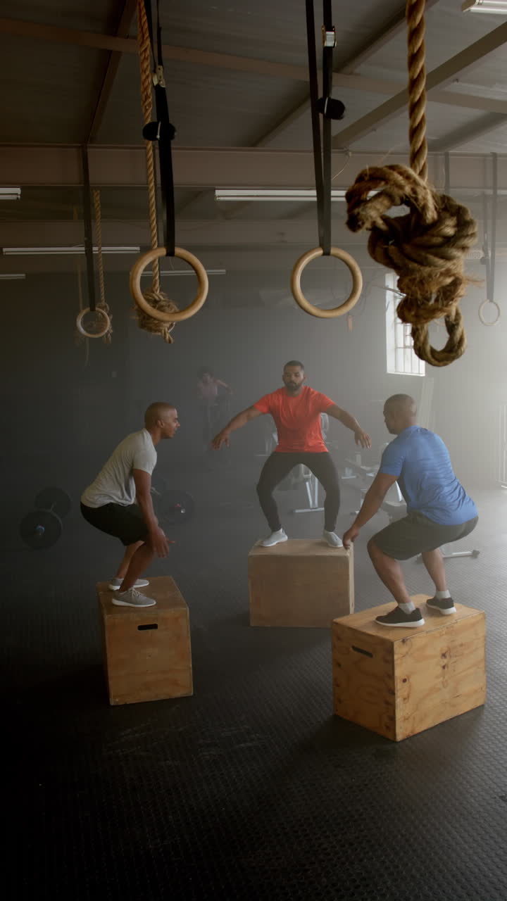 Vertical video of diverse sports people jumping on boxes at gym in slow motion