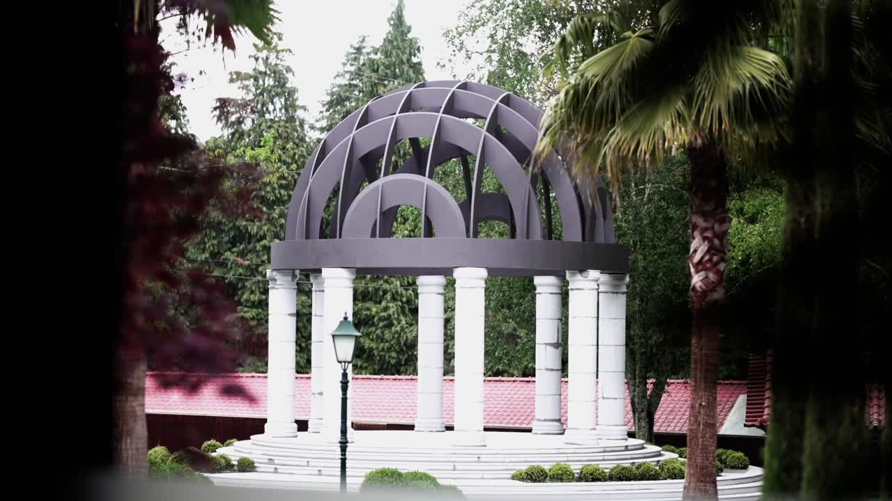 elegante gazebo de columnas blancas con cúpula negra moderna en un jardín exuberante