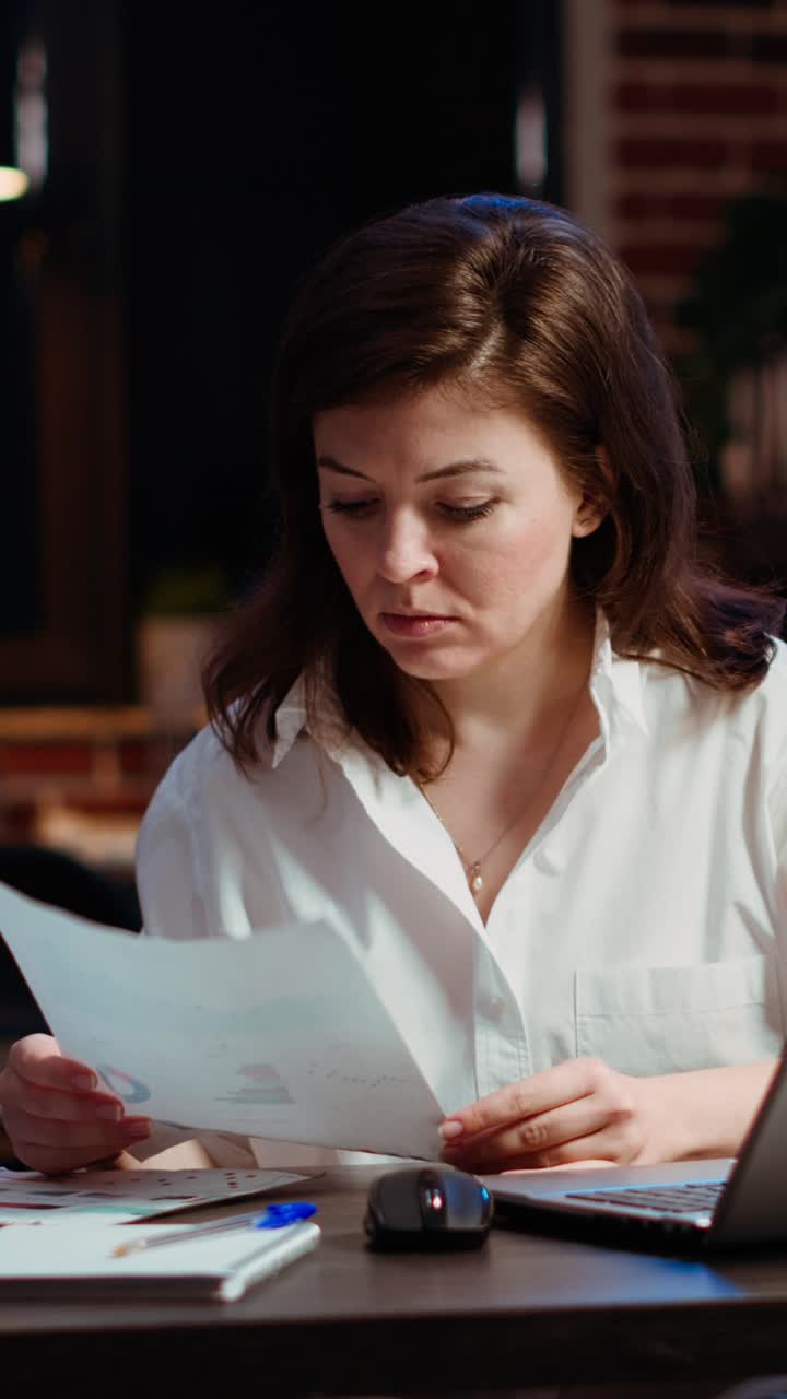 Vertical video Worker looking over paperwork containing financial graphs, researching data