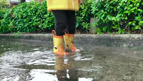child splashing in puddles while lightly raining wearing yellow boots. slow motion shot of rain.