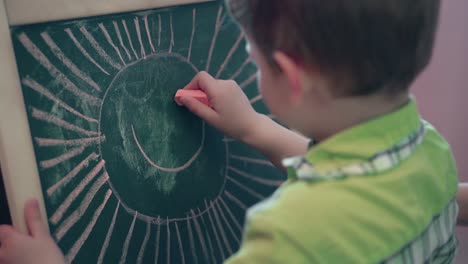little boy drawing on blackboard smiling sun