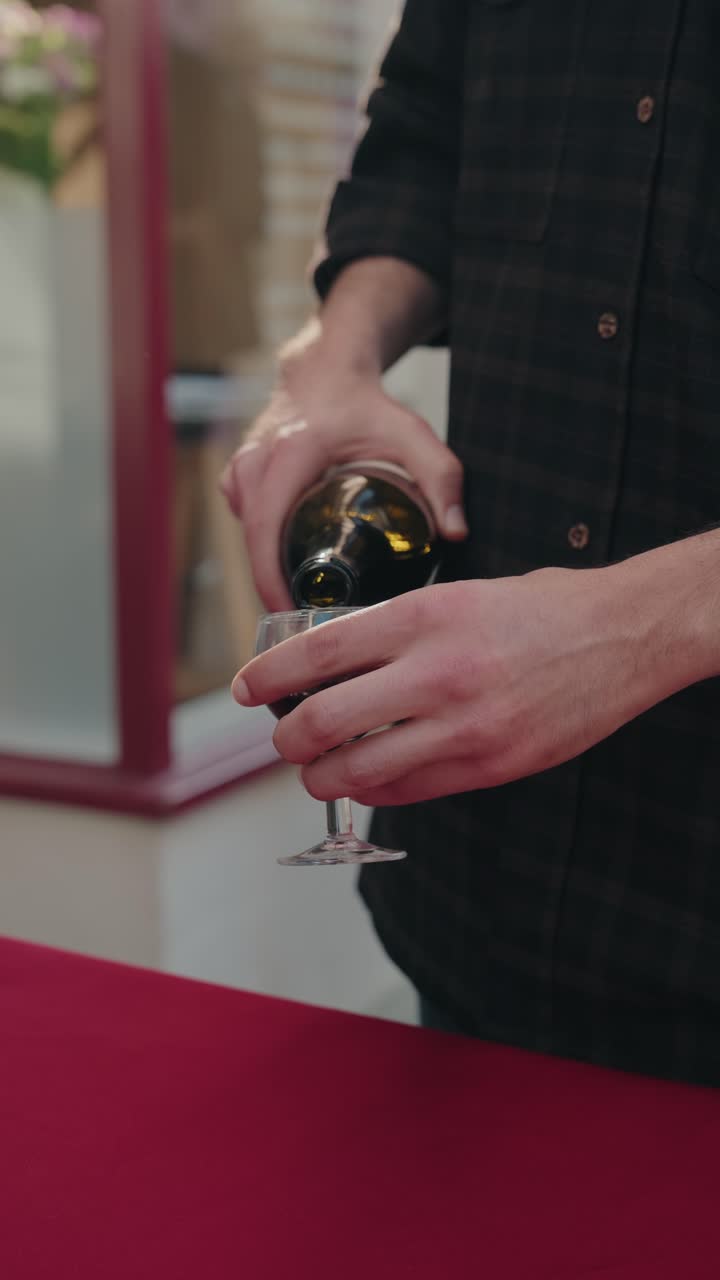 Verticaal aanzicht van handen die rode wijn uit een fles in een glas schenken