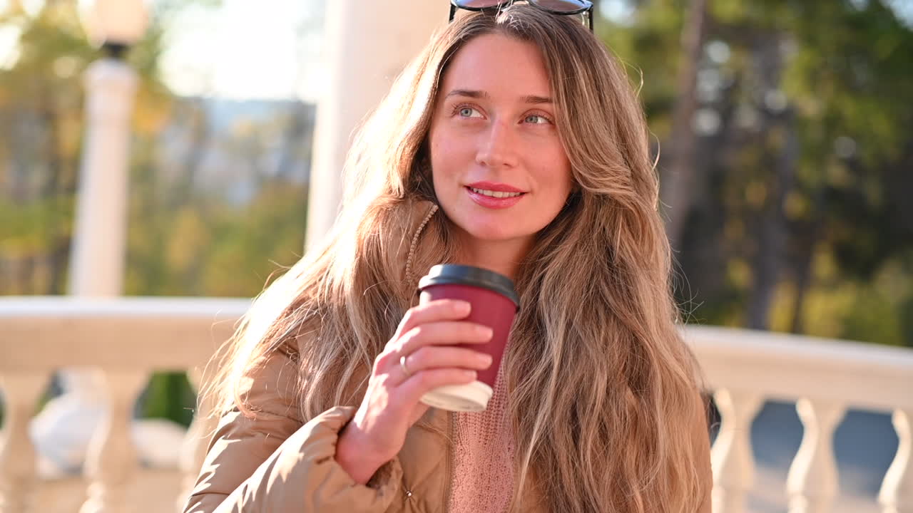 Woman drinking coffee and smiling in a park at sunset