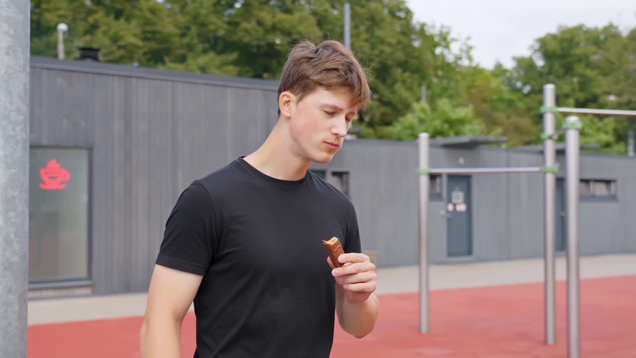 Athletic man chews protein bar with eyes closed while thinking calmly, soft daylight scene