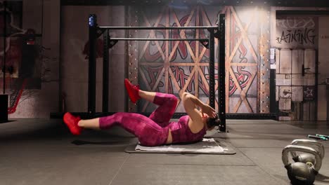 an athletic woman lies on a mat in a gym, performing bicycle crunches. this core exercise targets the abs and obliques for a complete abdominal workout