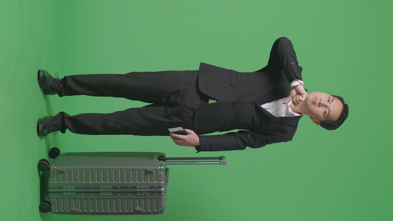 짐과 여권을 가진 아시아 사업가 여행자의 몸이 가득 차 있습니다. 카메라를 바라보고 녹색 화면 배경 스튜디오에서 엄지손가락을 아래로 표시합니다.