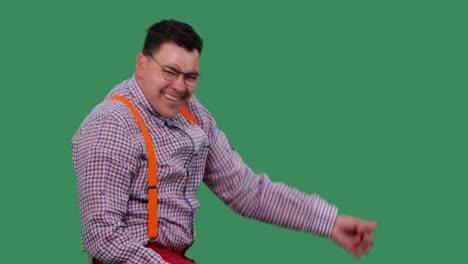 un hombre alegre con gafas baila, imitando tocar la guitarra. retrato de un hombre con una camisa a cuadros con tirantes naranjas en el estudio en una pantalla verde. cámara lenta. primer plano