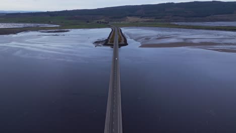 Top-down-view-of-the-Scottish-ocean-bridge-as-the-camera-pans-upwards,-revealing-a-picturesque-street-and-lush-green-landscape