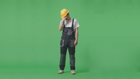 full body of asian man worker wearing goggles and safety helmet having a headache while standing in the green screen background studio