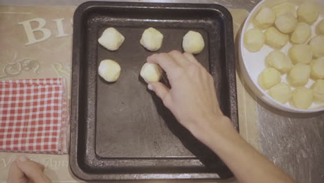 close up overhead footage of hands forming dough balls for chipa bread on a baking tray, showcasing the traditional baking process at home