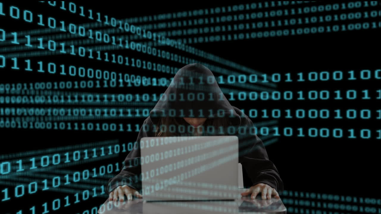 Hooded figure using laptop with binary code animation over dark background