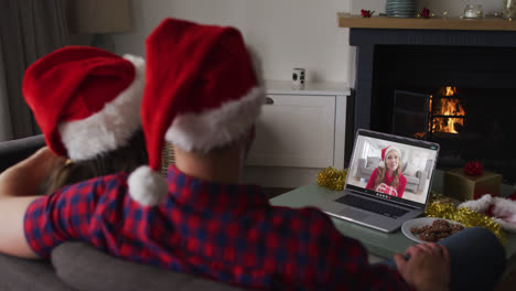 vista trasera de una pareja caucásica con sombreros de santa haciendo una videollamada en una computadora portátil durante la navidad