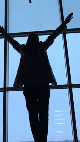 lady in jacket and trousers comes up to the panoramic window. dark female silhouette rises hands happily at the window. vertical video