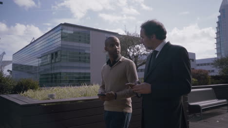 Serious-businessmen-with-smartphones-walking-near-office-buildings