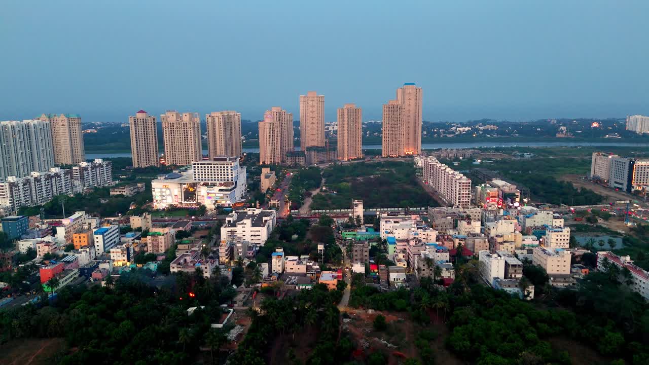 Aerial video of upscale residential development within a growing Indian city as night falls. numerous high-rise apartment towers with illuminated windows, showcasing contemporary design urban density