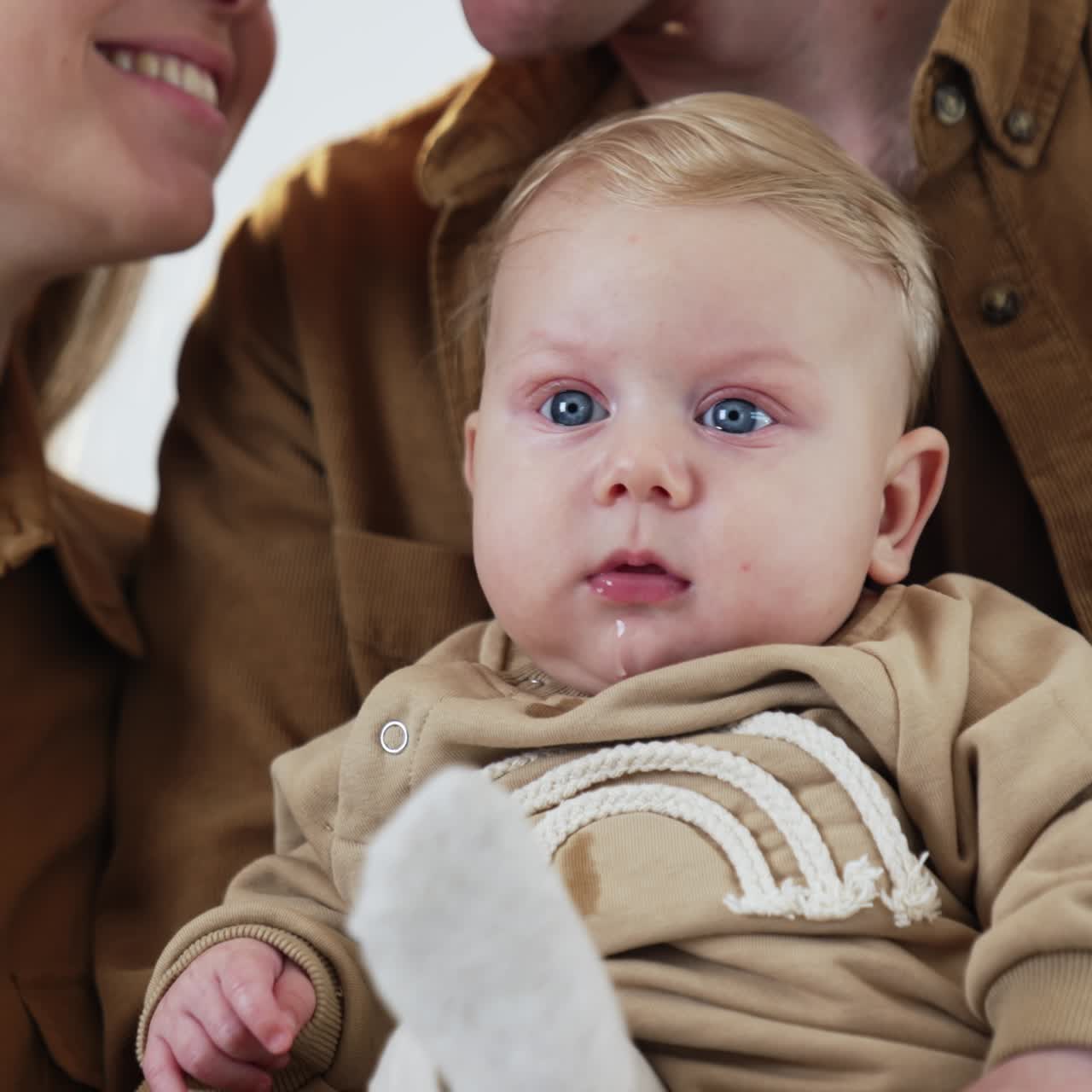 Adorable baby boy with blond hair and bog blue eyes. Little infant kid sitting comfortably in dad's hands. Close up