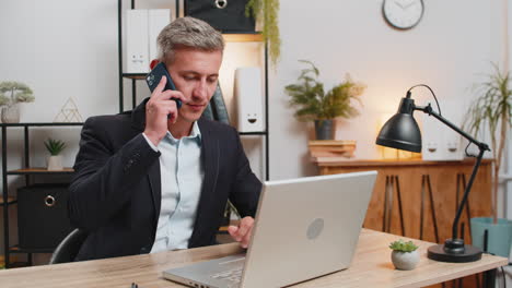 confident young entrepreneur using laptop and smartphone while working on project at home office