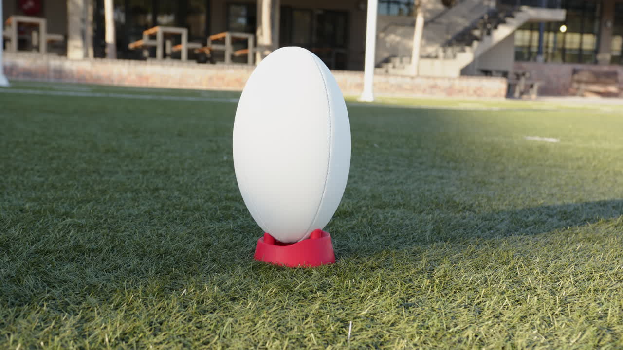 Rugby ball on red tee placed on green field, ready for kickoff, copy space
