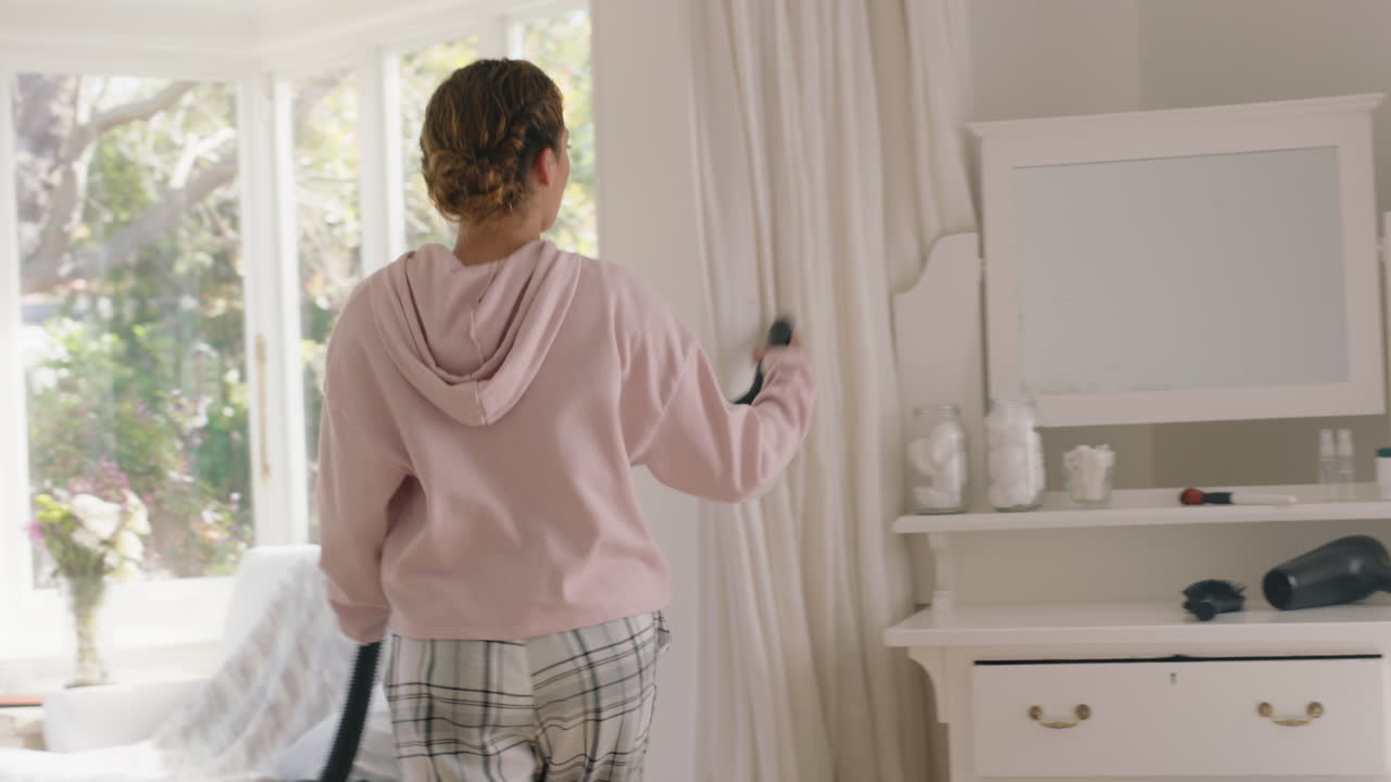 행복한 십대 소녀는 침실에서 진공청소기와 함께 춤을 추고 주말 아침을 즐기고 즐겁게 축하하고 집에서 피자마를 입고 무모한 라이프 스타일을 보내고 있습니다.