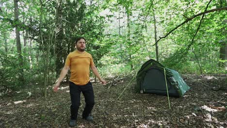 slow motion of man doing jumping jacks in forest campsite, front view near a green tent