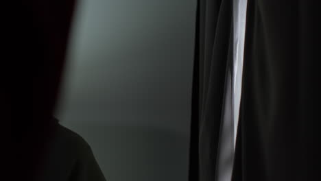 joven infeliz y deprimido en casa abriendo cortinas y mirando por la ventana 1