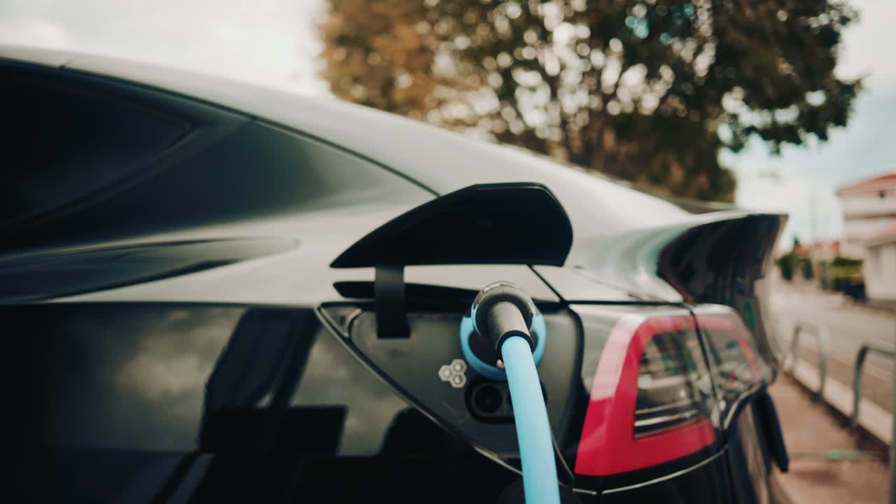 Şık siyah bir elektrikli arabaya bağlı bir şarj cihazının yakın çekim görüntüsü