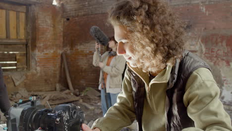 close up view of cameraman setting up a camera in a ruined building while anothers coworkers wating for start the recording 1