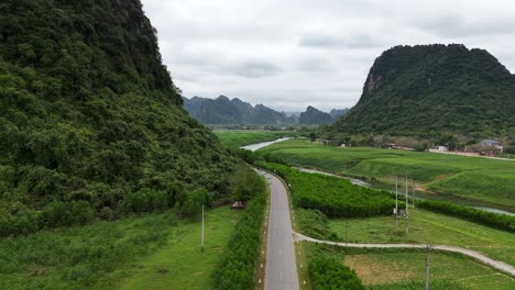 aerial drone shot of highway in the middle of crop field with mountain on the left and river passing nearby