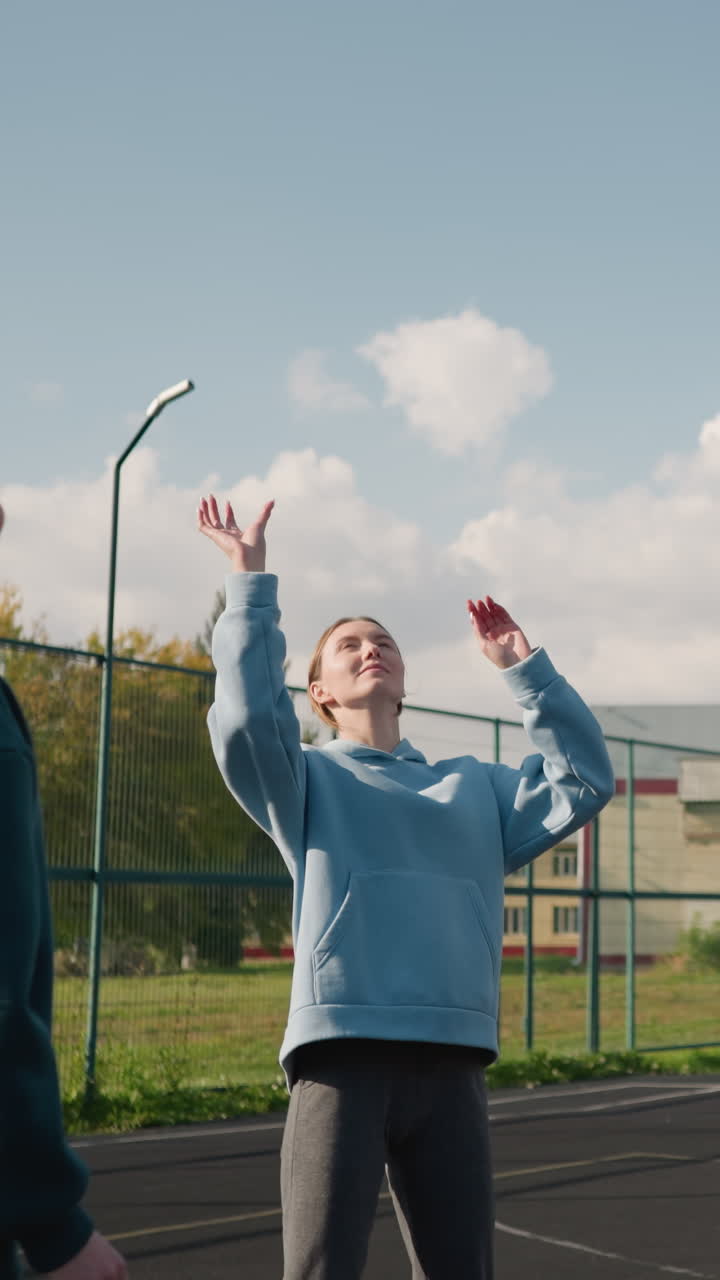 тренировочная сессия с тремя дамами, играющими в волейбол друг с другом, тренер в клетчатой рубашке вокруг талии, на открытом дворе с баскетбольным кольцом и забором на заднем плане