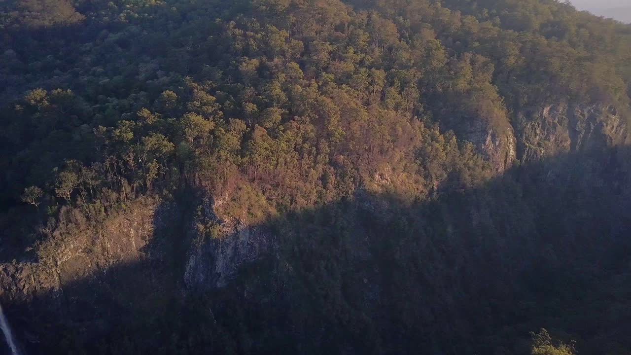Aerial cinematic view of Ellenborough falls in New South Wales, NSW, Australia. Slow circular motion around waterfalls during golden hour, dark and moody landscape wilderness with shade