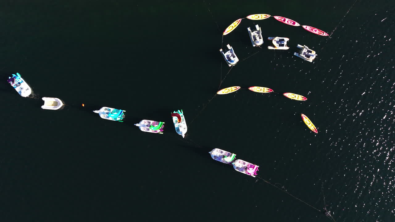 Drone view of colorful pedal boats floating in formation on lake water