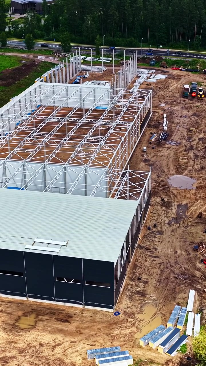 Struttura in acciaio che si innalza in un cantiere di data center vicino a un distretto industriale, inquadratura aerea verticale dopo una giornata di pioggia.