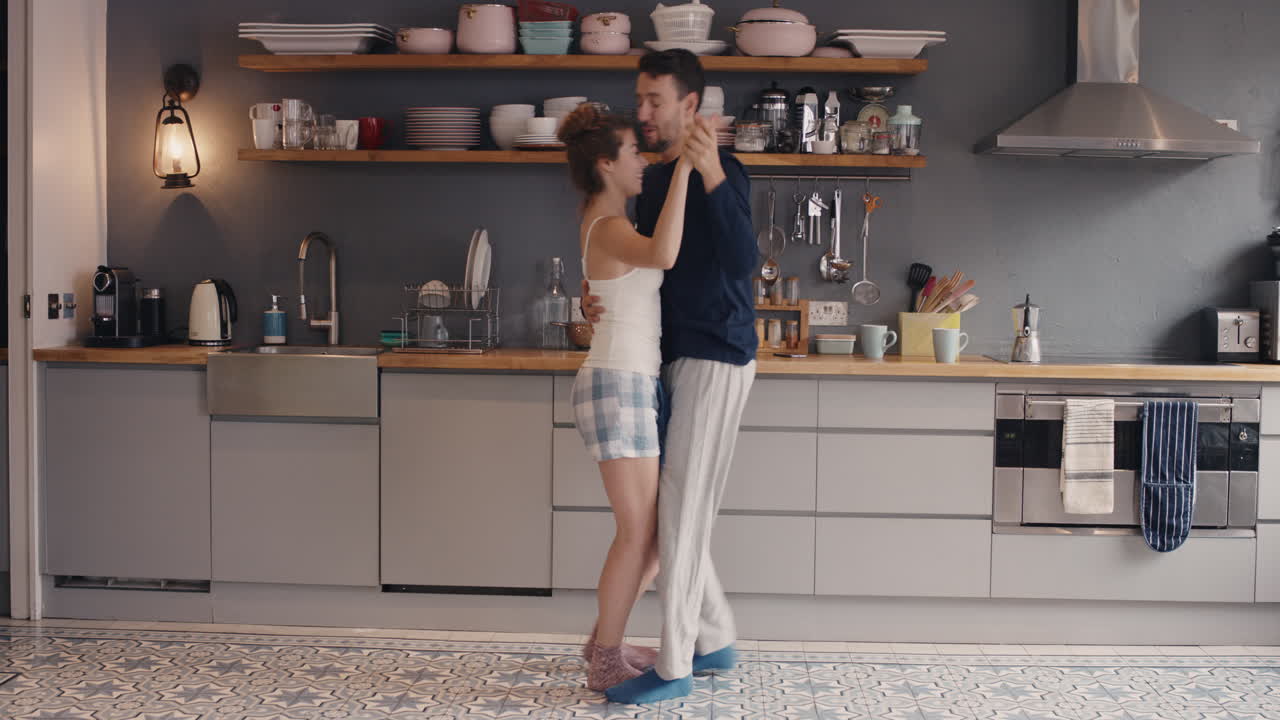 Giovane coppia felice di novelli sposi che balla e ascolta musica in cucina, vestita, al mattino a casa.