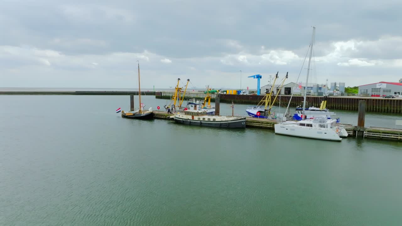 Borkum harbor with docked boats under cloudy sky, aerial drone view, pan left orbit.