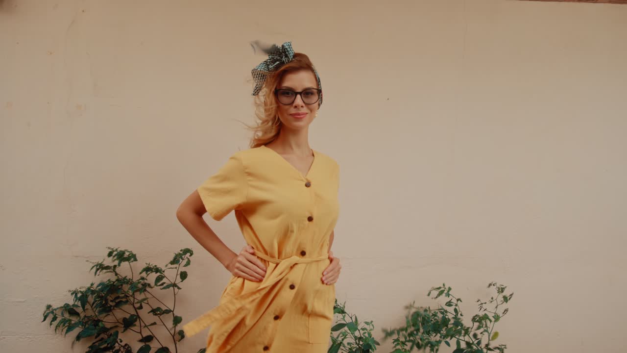 A stylish woman in a yellow dress and glasses posing outdoors