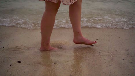 disparo en cámara lenta de una persona femenina caminando por la orilla de la playa de arena