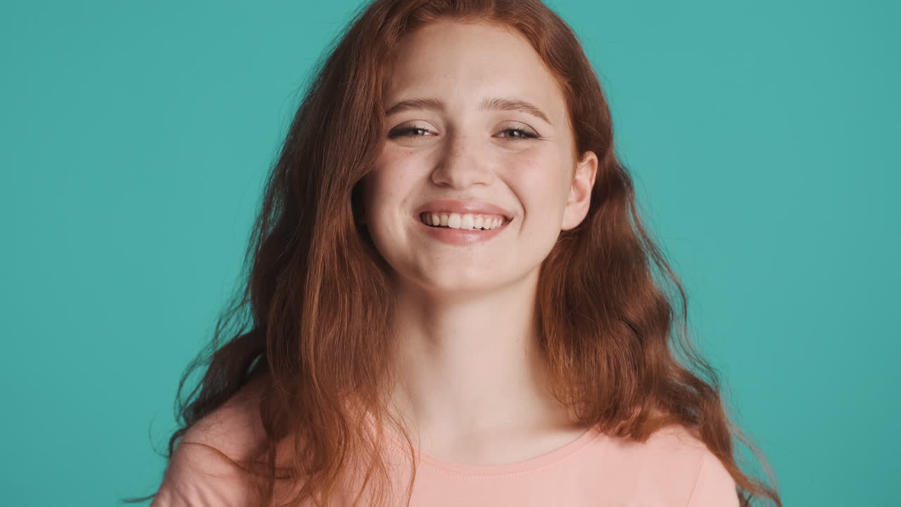 Redheaded girl in front of camera on turquoise background.