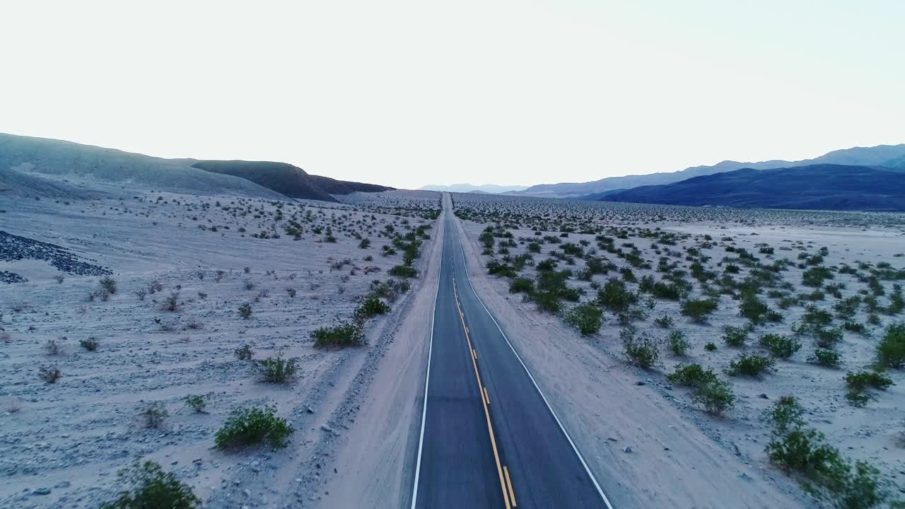 Drone moves backward over an endless desert road in Death Valley at sunrise, 4K