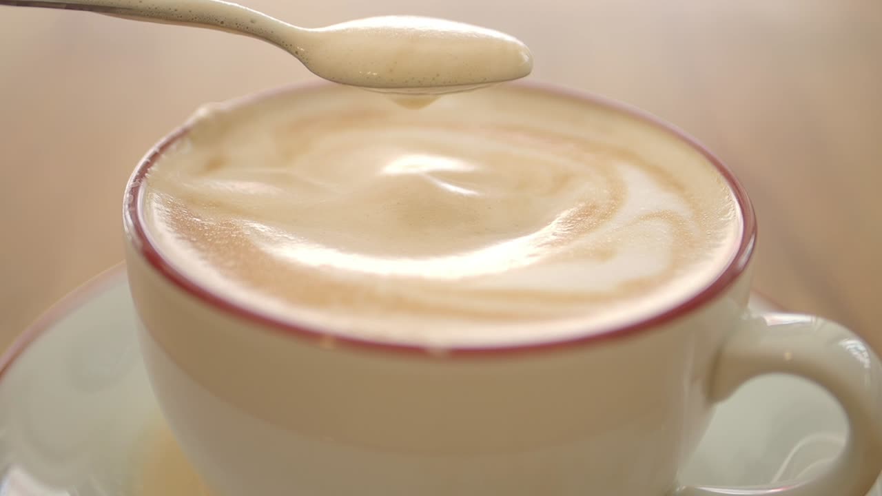 カプチーノカップの中でスプーンが泡をかき混ぜるクローズアップ