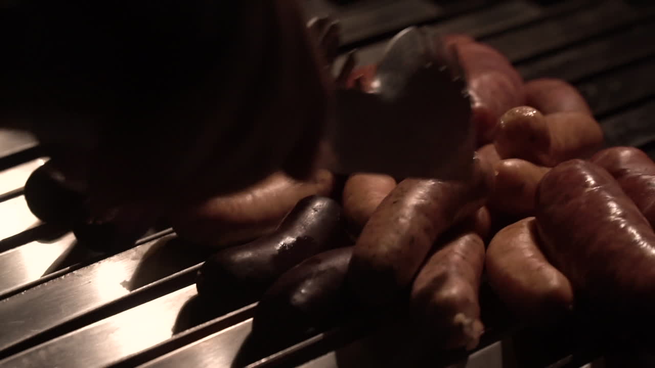 Hand with tongs to accommodate sausages being fried on a brick barbecue grill DETAIL SHOT