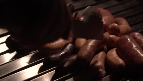 hand with tongs to accommodate sausages being fried on a brick barbecue grill detail shot