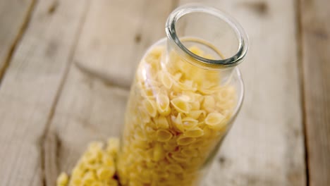 Pasta-Conchiglion-Ordenada-En-Frasco-Y-Esparcida-Sobre-Mesa-De-Madera