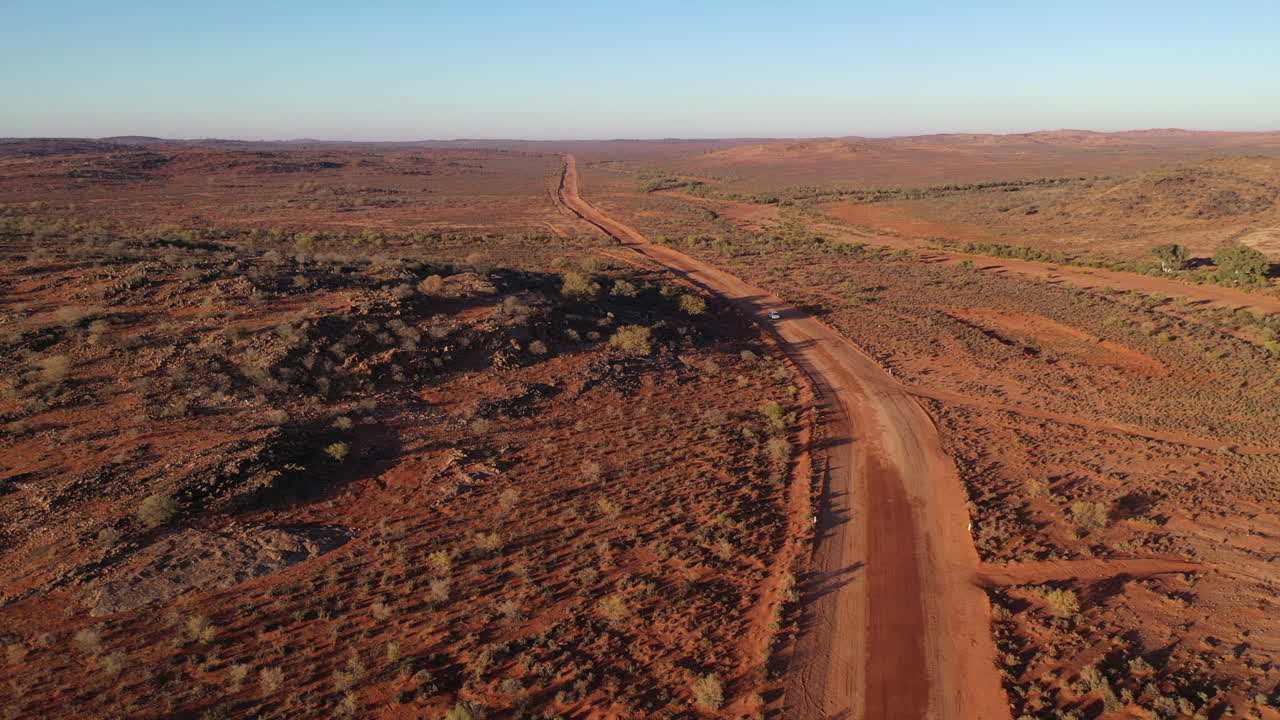 Aerea: Ripresa con drone che segue un veicolo che percorre una strada vuota nell'outback australiano verso l'orizzonte vicino a Broken Hill, Australia.