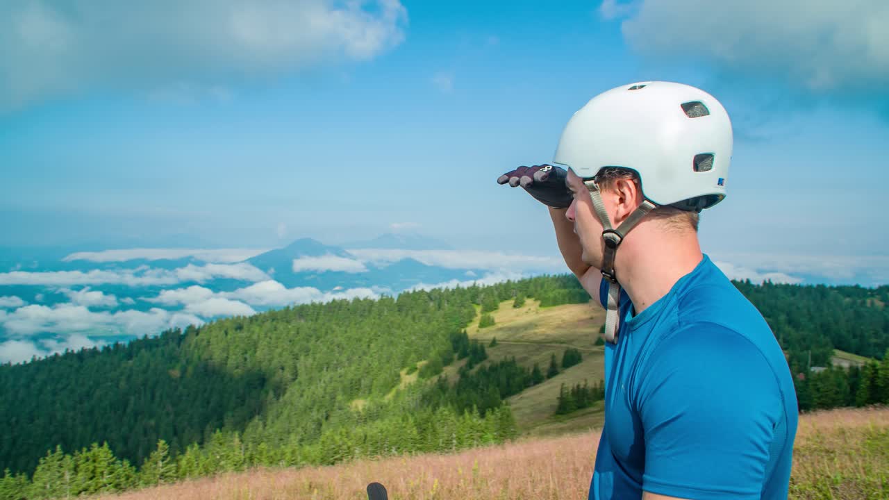 Circle dolly shot male cyclist with helmet looking out landscape view, mountains and clouds, Medium shot